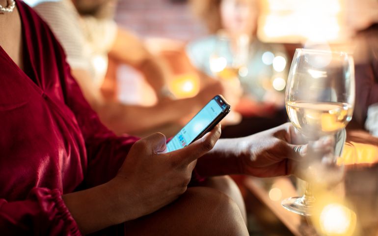 Young woman using a phone while having a glass of wine