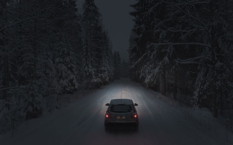 Driving a car on a forest snowy road at night. Headlights light the way