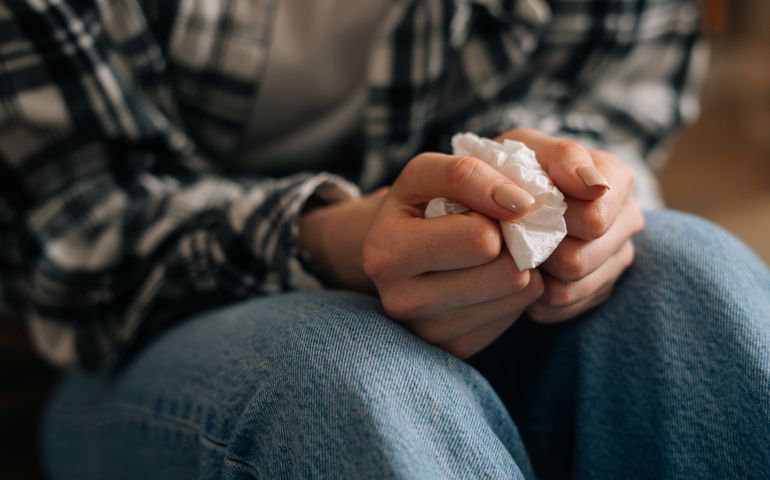 shot of unrecognizable crying young woman holding paper tissues in hands and nervously rummaging through them at home.