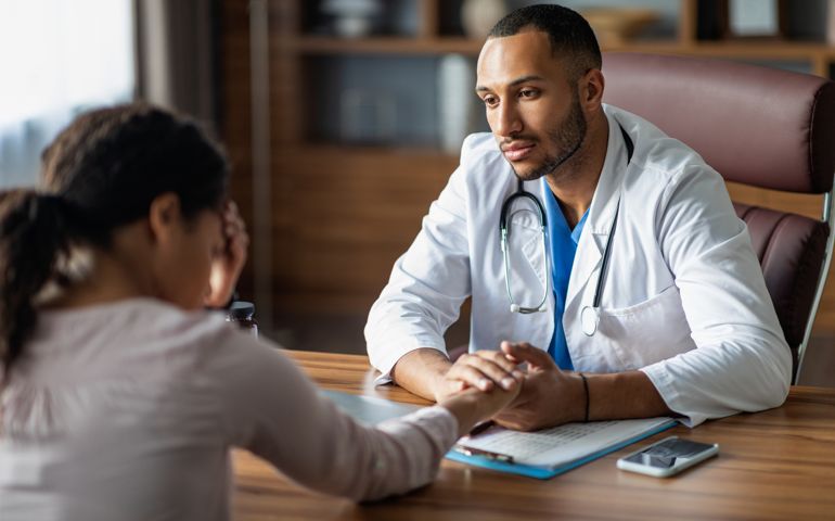 Doctor having conversation with upset black woman patient, holding hand