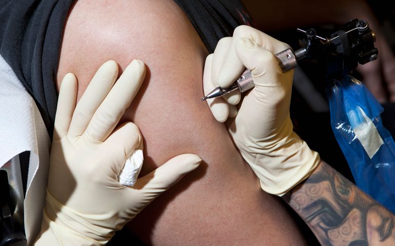 A tattoo artist preparing to tattoo a man's bare arm, close-up