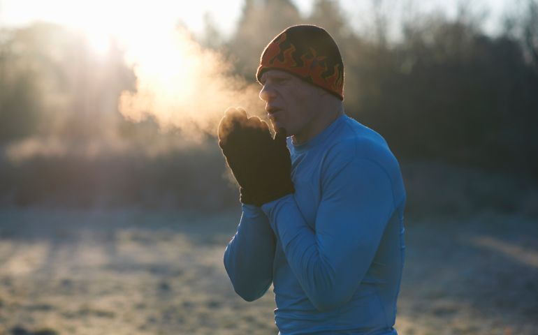 Runner wearing knit hat and gloves, rubbing hands together, breathing cold air