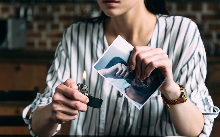 cropped shot of young woman burning photo card of ex-boyfriend