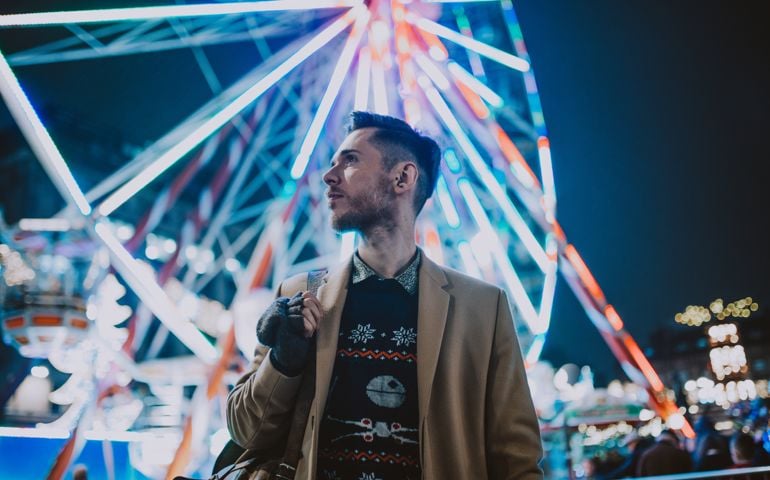 Stylish young man at a carnival/funfair standing in front of a big wheel