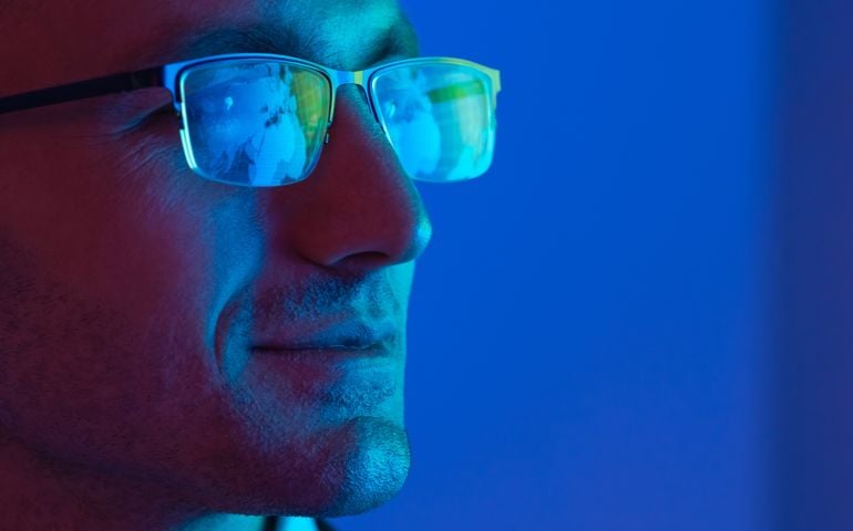 man with glasses staring at blue screen