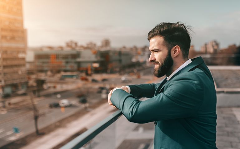 Profile of bearded businessman leaning on the fence and looking at view while standing on rooftop.