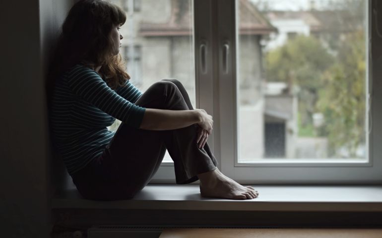 Sad young woman sitting on the window, watching out