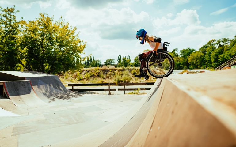 millennial woman in wheelchair rolls down the hills in skate park