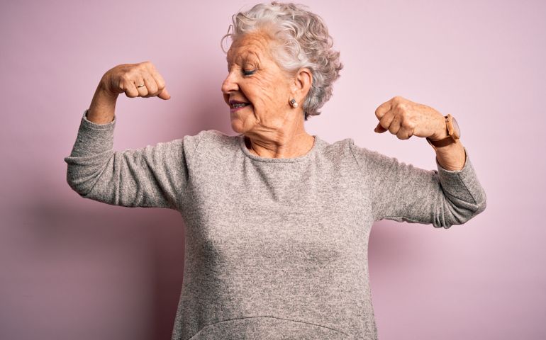 Senior beautiful woman wearing casual t-shirt standing over isolated pink background showing arms muscles smiling proud. Fitness concept.
