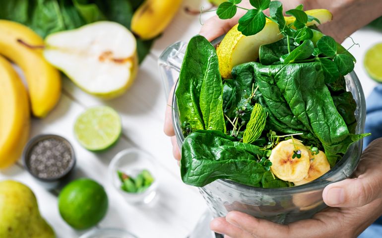 Woman is preparing a healthy detox drink in a blender - a smoothie with fresh fruits, green spinach and superfood seeds. Healthy lifestyle concept, ingredients for smoothies on the table, top view