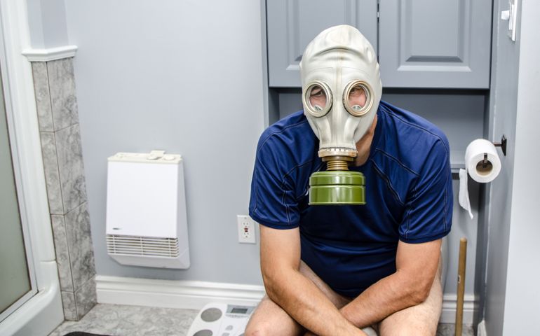 Adult man sitting on toilet with gas mask