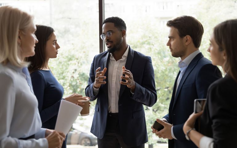Confident African male leader telling diverse colleagues about new project
