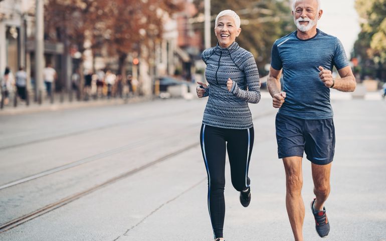 Senior man and senior woman jogging side by side on the street