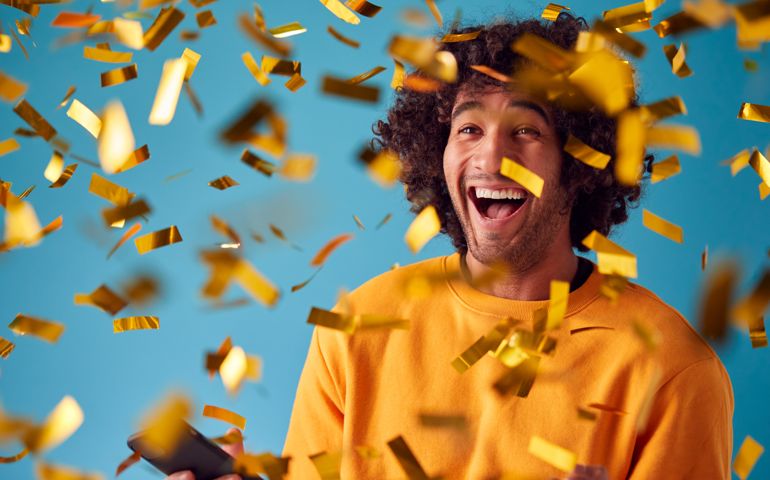 Celebrating Young Man With Mobile Phone Winning Prize And Showered With Gold Confetti In Studio