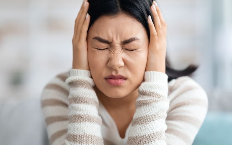 Emotional Asian Woman Covering Ears With Hands At Home