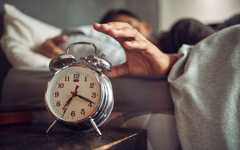 Shot of a young man reaching for his alarm clock after waking up in bed at home
