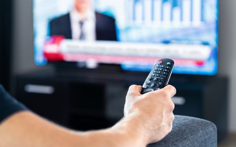 Man watching tv news program and sitting on couch home. Television remote control in hand. Politics, business or finance network channel. Online live broadcast in monitor screen.
