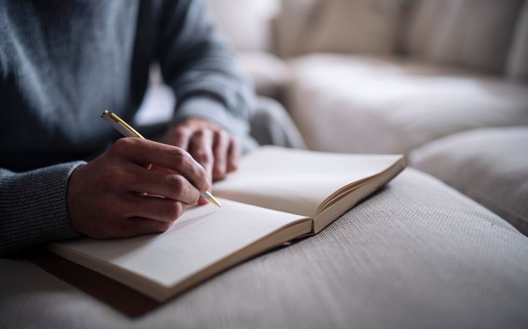 Cropped hand of man writing in notebook.