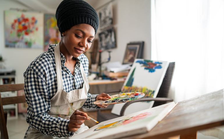Afro female fine artist with traditional african hat and apron, drawing in art studio
