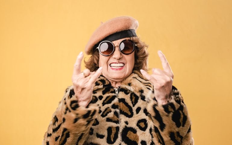 Stylish senior woman showing rock n roll gesture while posing on isolated background.
