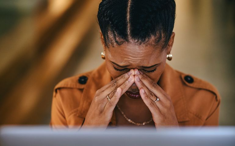 Tired and stressed businesswoman with a headache from burnout of working and looking at her laptop screen. Frustrated female manager sad and crying at her desk in her modern office in the evening