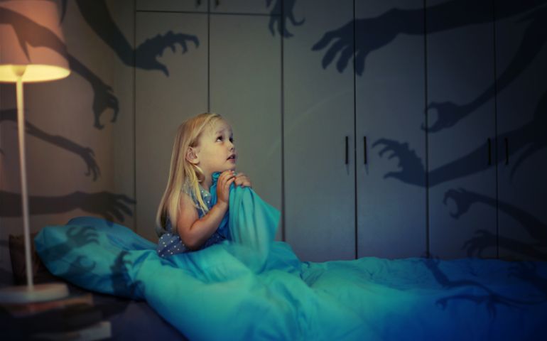 child sitting on bed looking towards wall with shadow figures