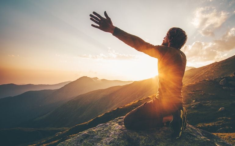 Man praying at sunset mountains raised hands Travel Lifestyle spiritual relaxation emotional concept vacations outdoor harmony with nature landscape
