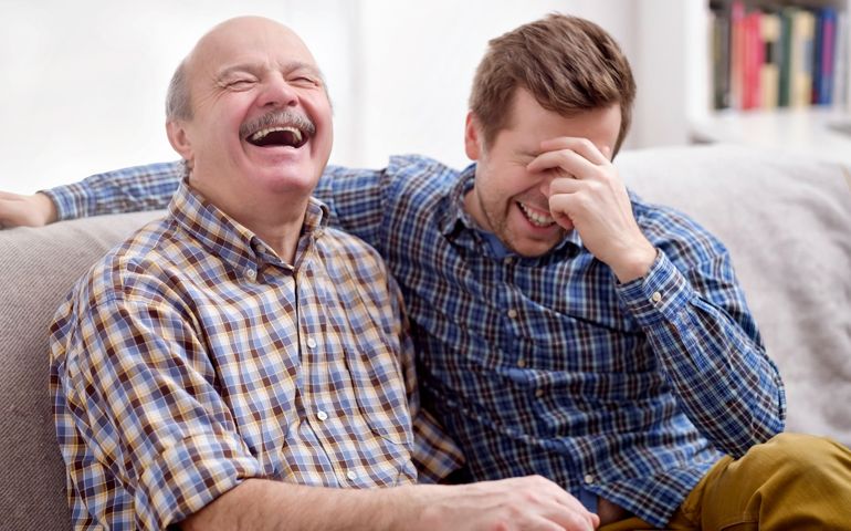 Father and son are sitting on the sofa in the living room and remember joke