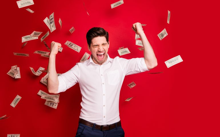 Photo of ecstatic overjoyed man rained with bucks banknotes achieving success while isolated with red background