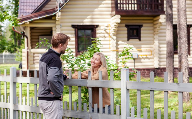 Middle aged man meeting smiling female neighbor in countryside and talking cheerfully to her over fence