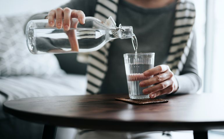 Close up of young Asian woman pouring water from bottle into the glass on a coffee table at home. Healthy lifestyle and stay hydrated