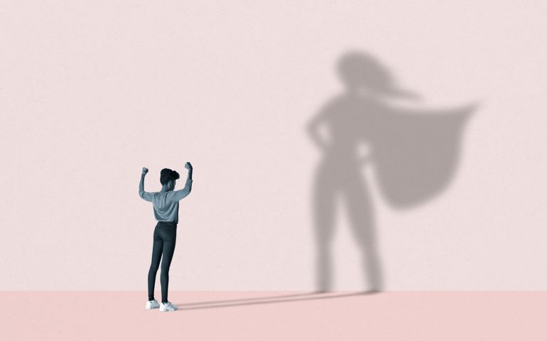Woman flexing muscles in front of superhero shadow