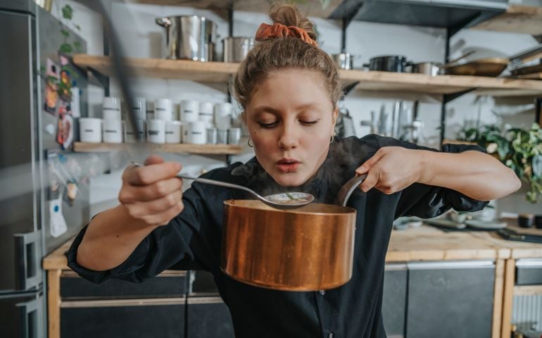 Young female chef tasting Broth soup while standing in kitchen
