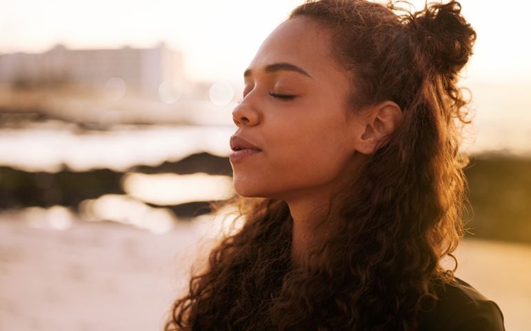Shot of an attractive young woman sitting alone on a mat and meditating on the beach at sunset