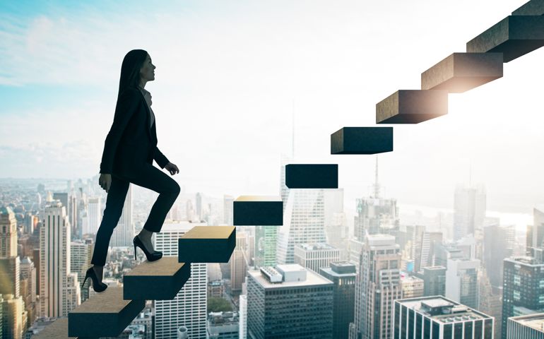 Road to success concept with businesswoman going up the stairs on sunny megapolis city background.
