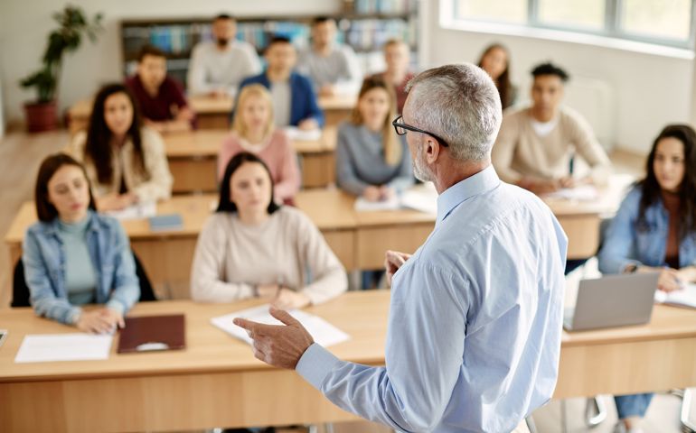 Rear view of mature teacher talking to his student during lecture at university classroom.