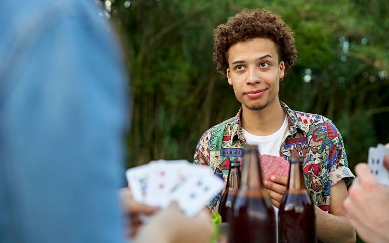 Young man enjoying beer and cards outdoors with friends