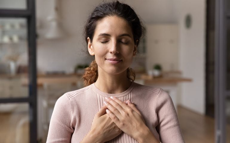 Calm young woman hold hands on chest praying