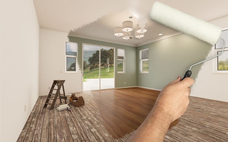 Before and After of Man Painting Roller to Reveal Newly Remodeled Room with Fresh Light Green Paint and New Floors.