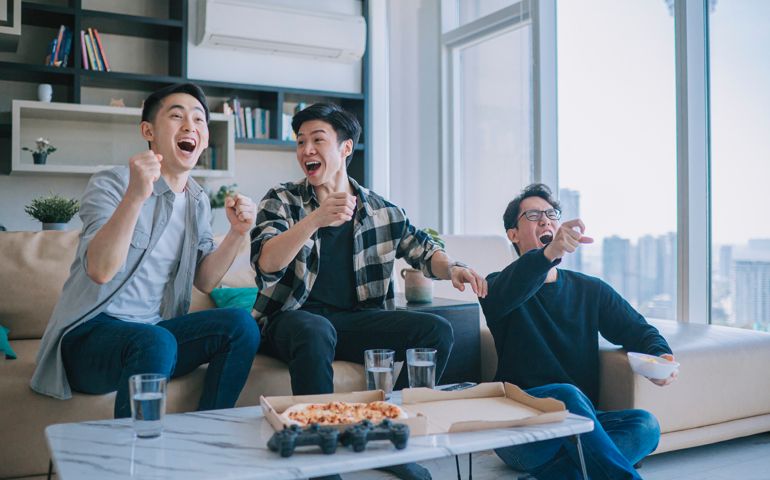 Asian Chinese young man shouting and cheering for his team support while watching sports on tv from home with his friends. Celebrate Victory when Sports Team Wins Championship. Friends Cheer, Shout