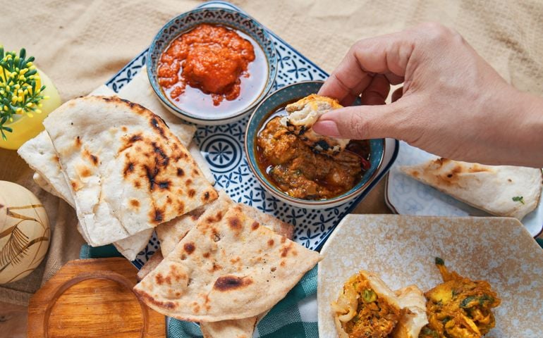 A hand dipping roti on the butter chicken