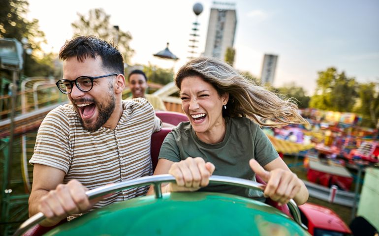 Young cheerful couple having fun on rollercoaster at amusement park.