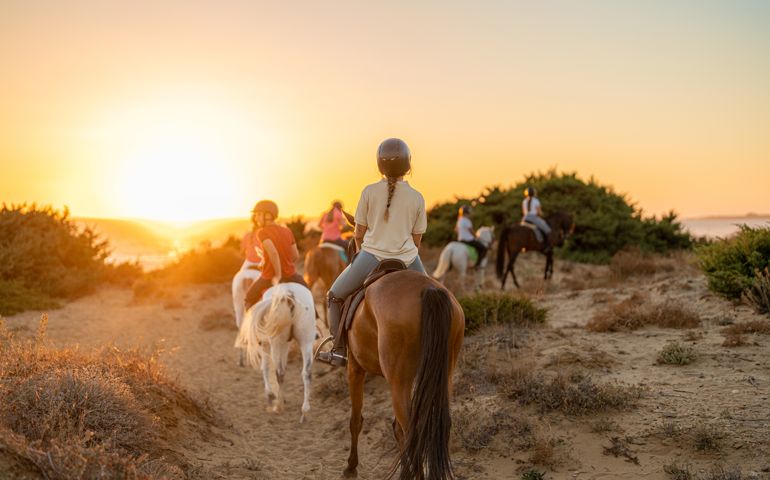 group of young riders on horseback heading towards the beach