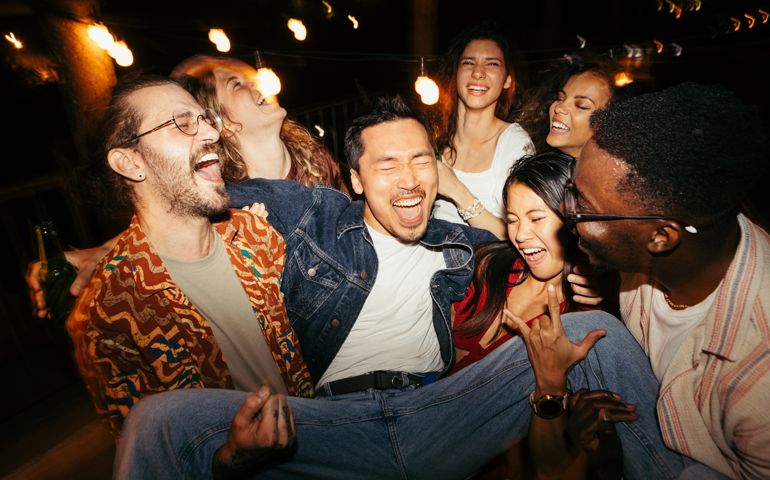 Friends lift their male friend at the night open-air rooftop party.