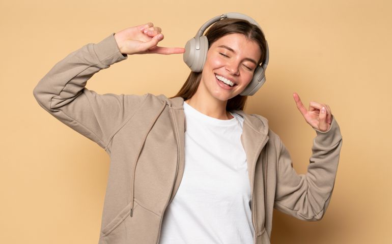 Millennial girl in hoodie enjoying song moving to rhythms while listening to music in headphones