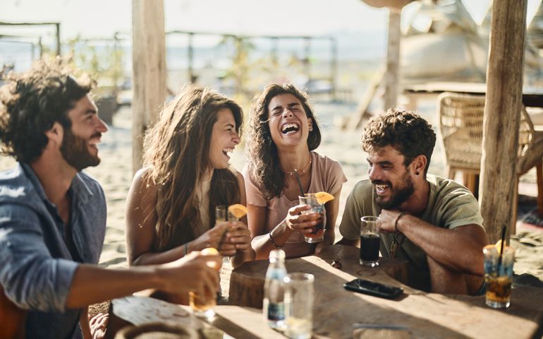 Cheerful couples talking in summer day at a beach bar.