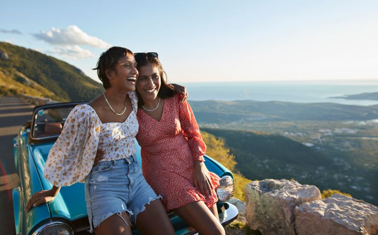 Woman with arm around female friend leaning on car