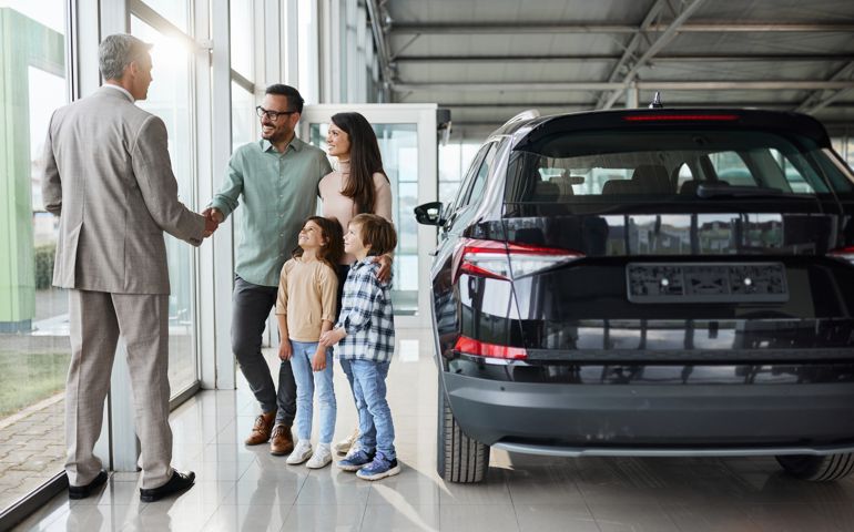 Young happy family shaking hands with a car salesperson in a showroom.