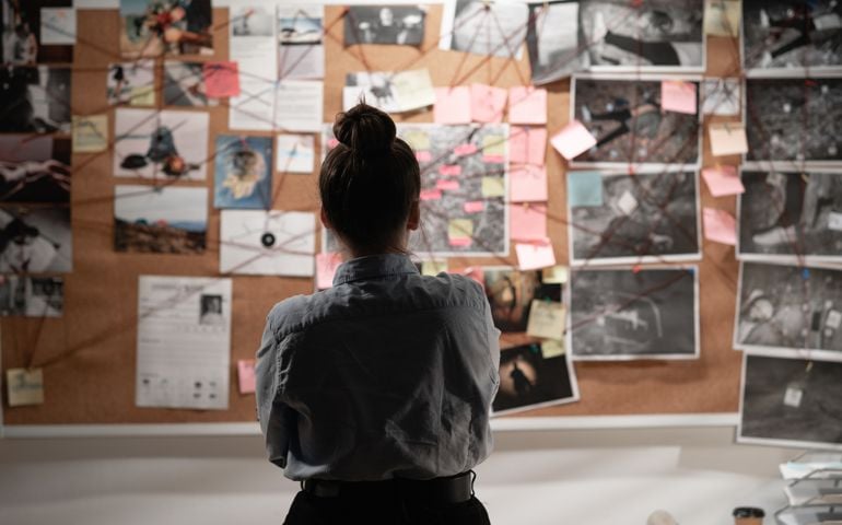 Female detective looking attentively at investigation board, back view.