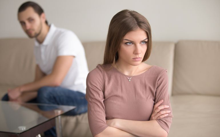 Angry sad woman standing with arms crossed, man in background